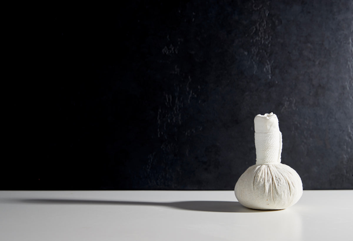 Small cream-colored fabric massage ball with gathered top and ridged surface against dark background.