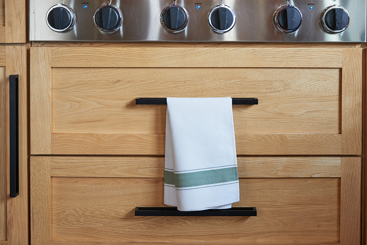 White kitchen towel with green herringbone stripe band draped over oven door handle.