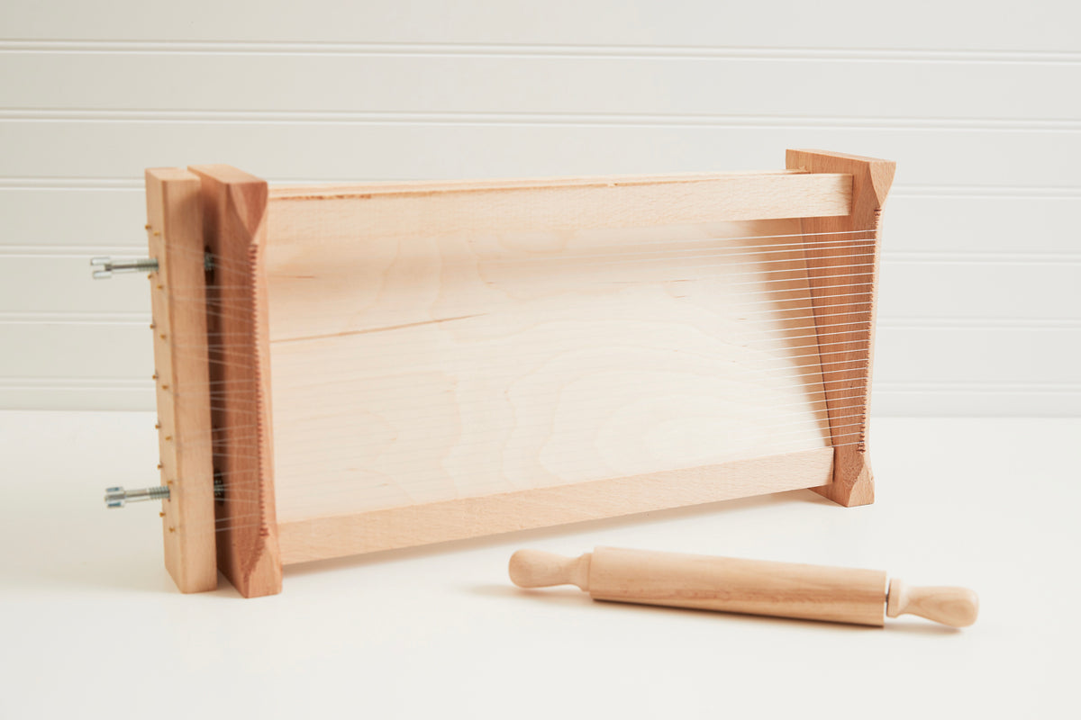 Wooden pasta chitarra with parallel metal strings and matching wooden rolling pin with handles.