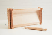 Wooden pasta chitarra with parallel metal strings and matching wooden rolling pin with handles.