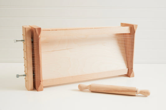 Wooden pasta chitarra with parallel metal strings and matching wooden rolling pin with handles.