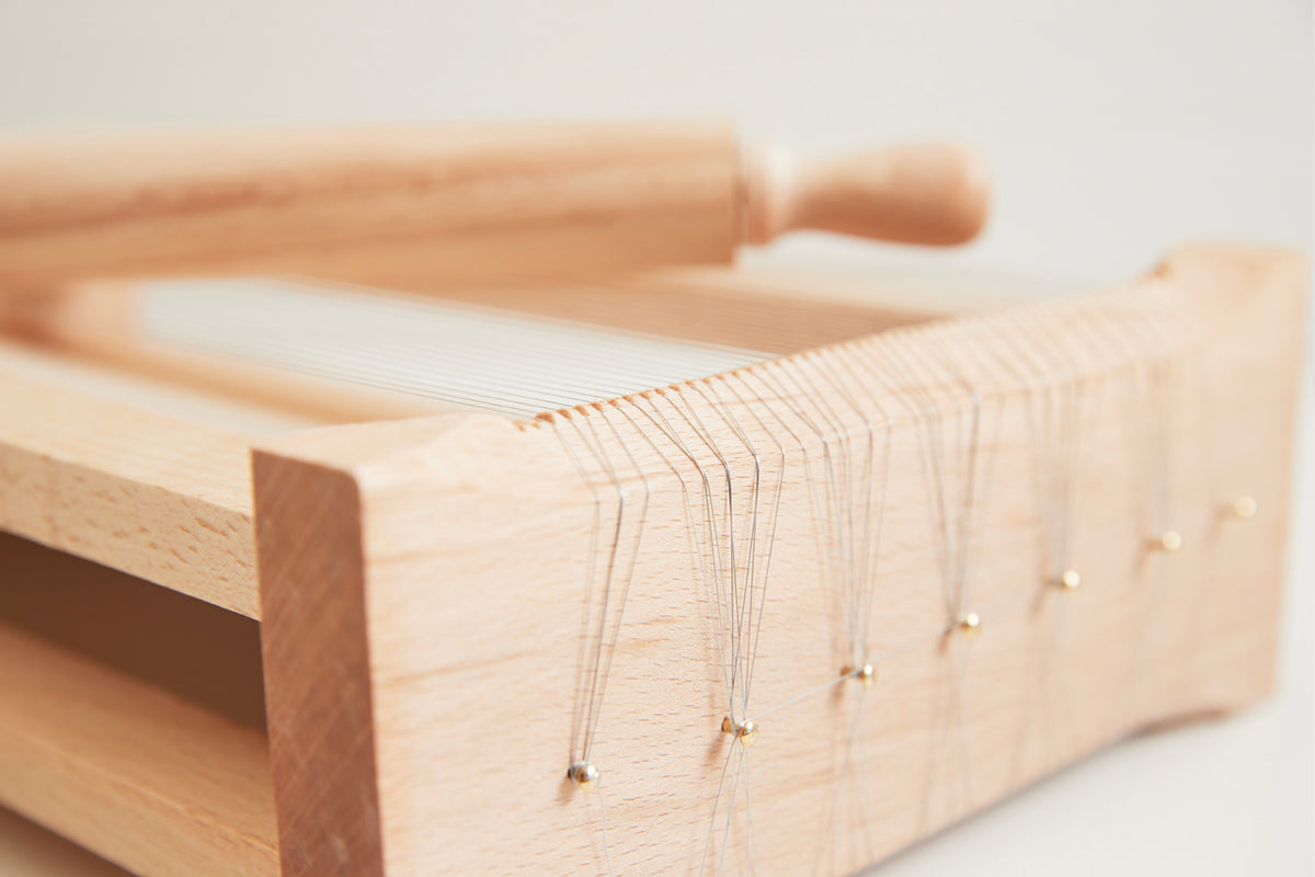 Wooden pasta chitarra with parallel strings and rolling pin on white background.
