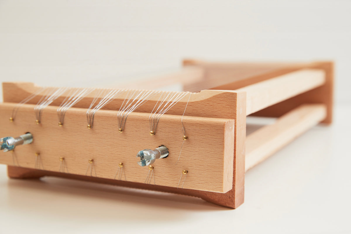 Wooden pasta chitarra with metal strings and rolling pin, viewed from the side on white background.