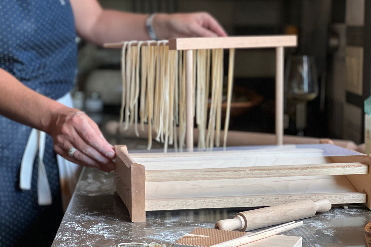 Wooden pasta chitarra with fresh pasta strands hanging from the frame and rolling pin positioned beside it.