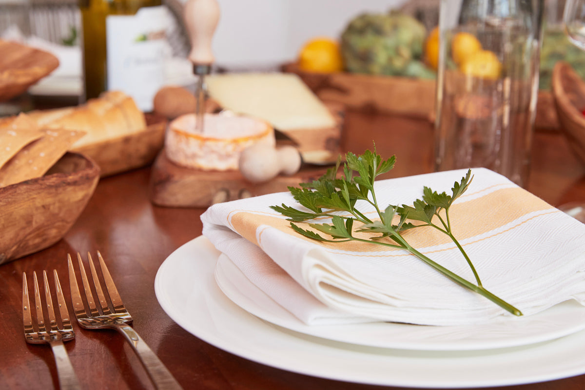 Cream and tan herringbone kitchen towel folded on white plate with fresh parsley sprig in Italian table setting.