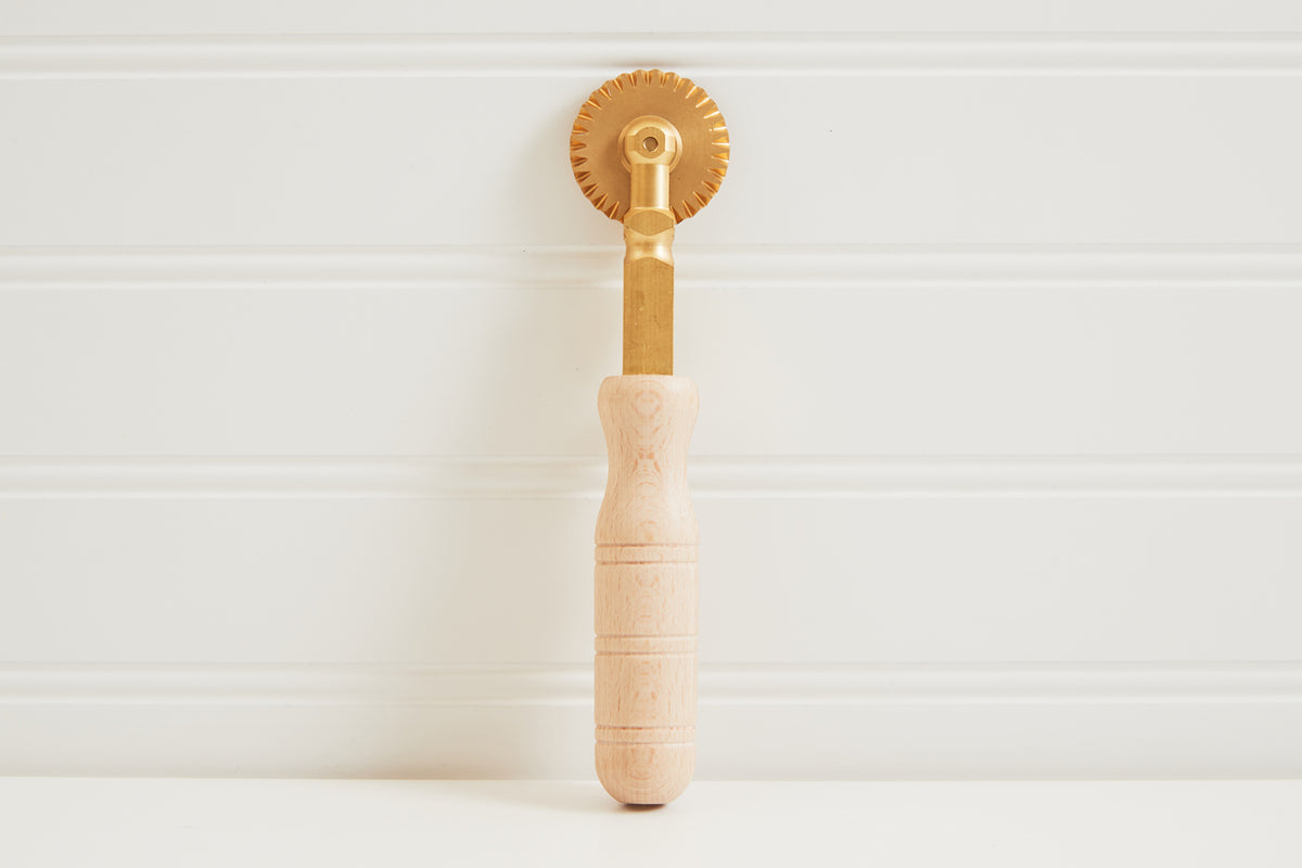Brass pasta wheel with fluted cutting edge and natural wood handle with grip rings.