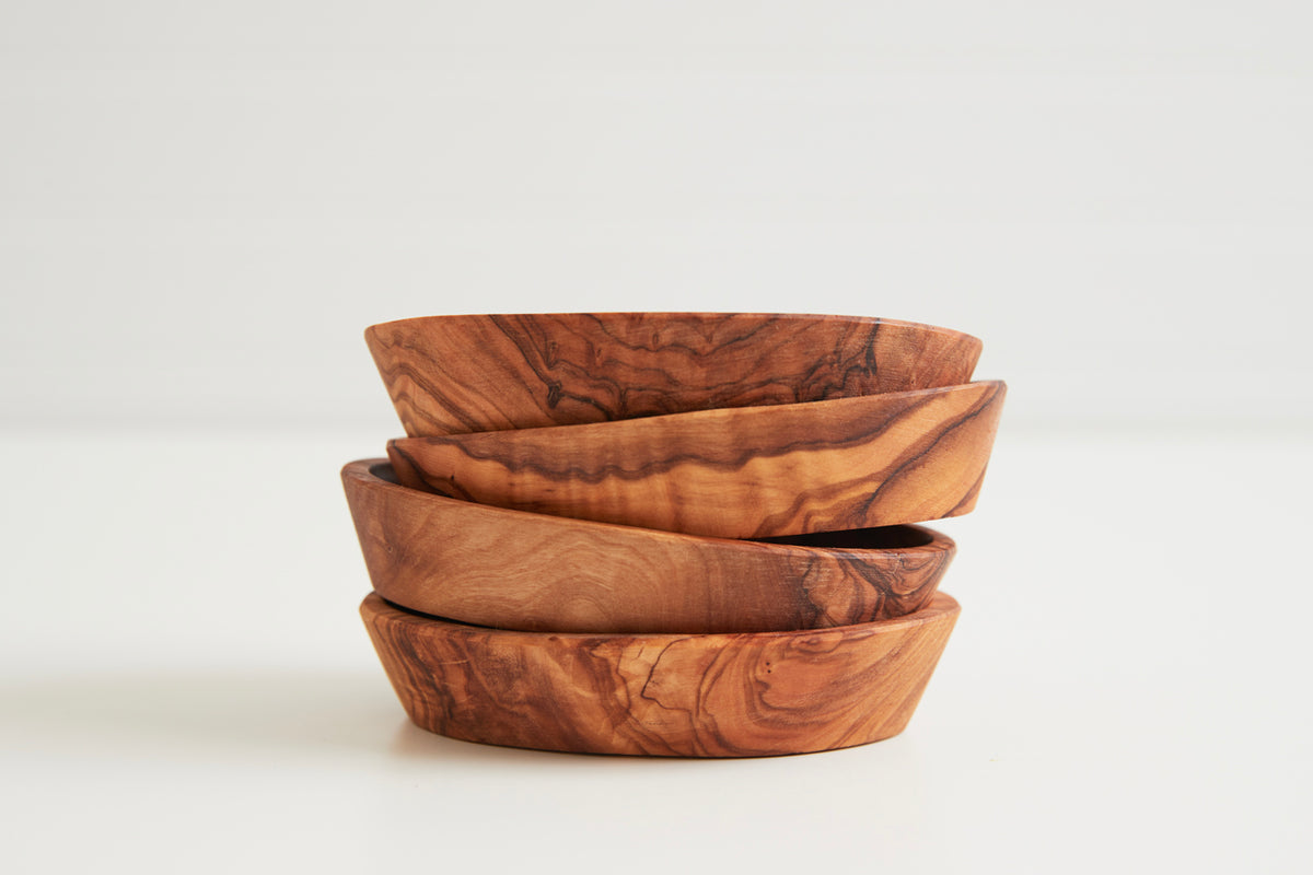 Four stacked wooden bowls with natural grain patterns in varying shades of brown and tan.