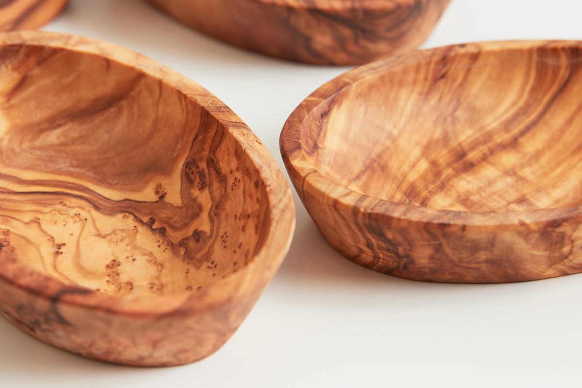 Four shallow wooden bowls with natural grain patterns and warm brown tones.