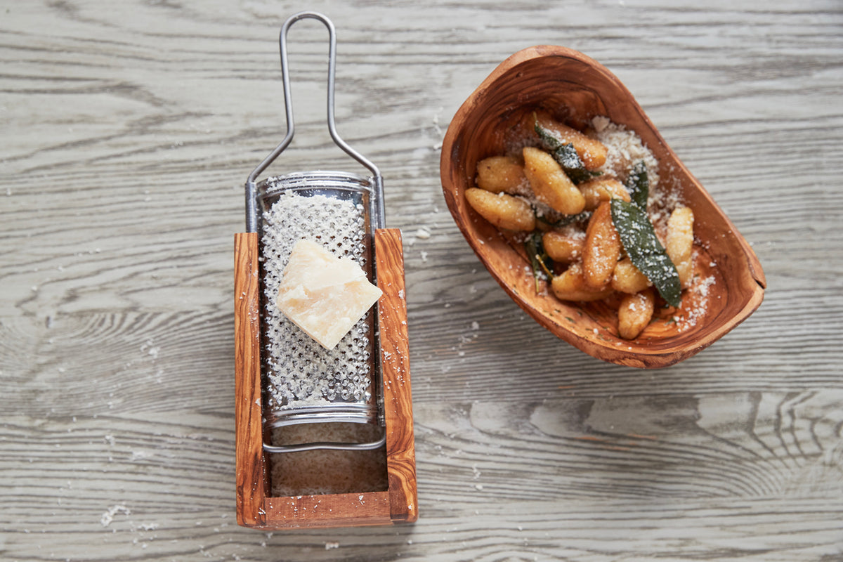 Box grater with olivewood base and metal grating surface, displayed with grated cheese and a wooden bowl of croutons.