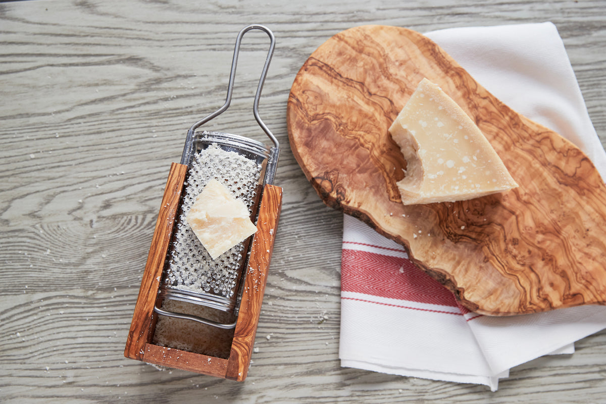 Olivewood box grater with metal grating surface and wooden handles, displayed with grated Parmesan cheese and wooden serving 