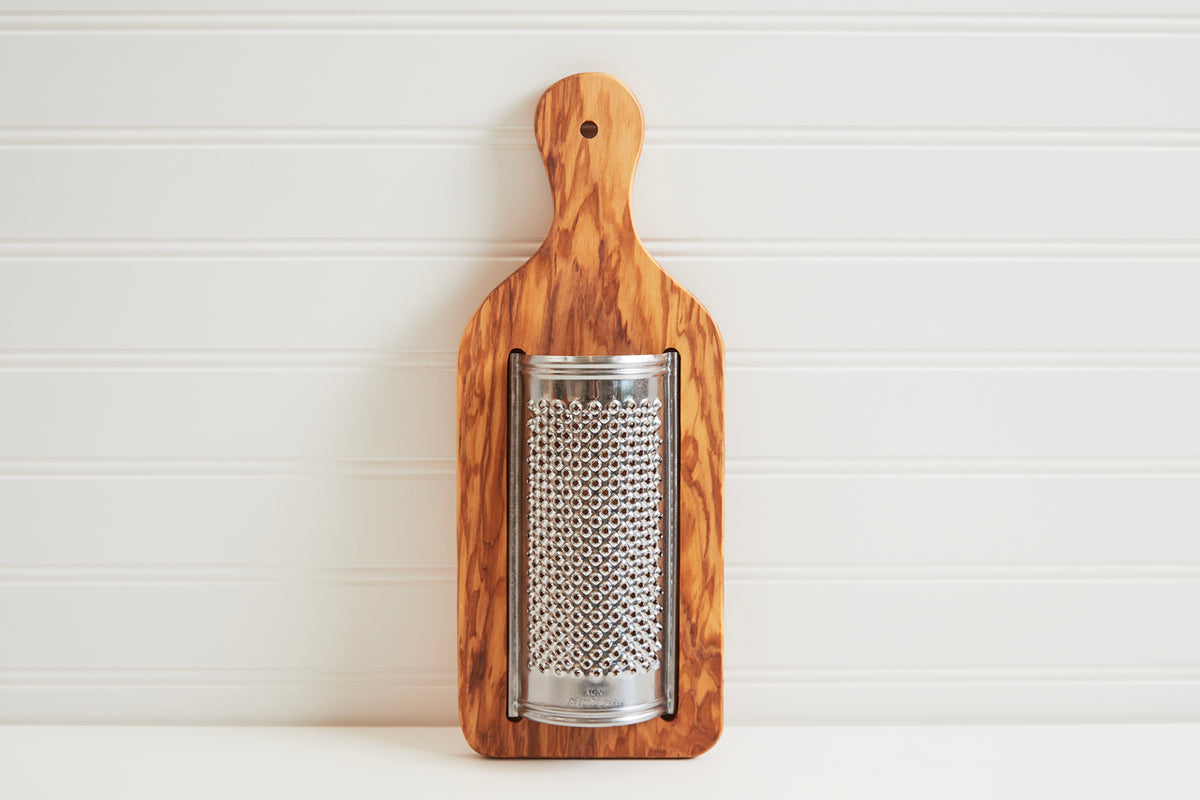 Flat cheese grater with olive wood handle and metal grating surface with circular perforations.