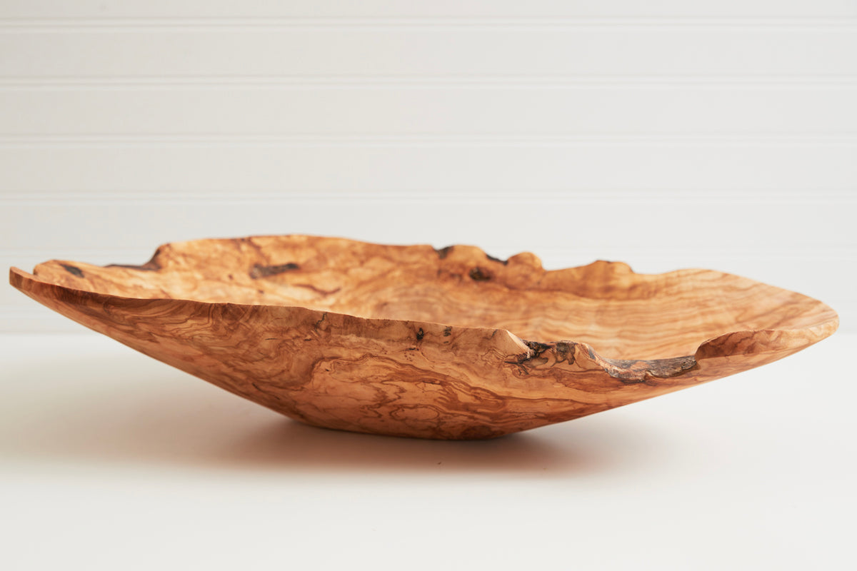 Shallow wooden bowl with natural grain patterns and irregular wavy edges on neutral background.