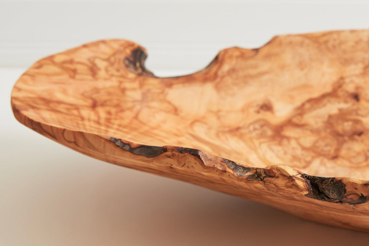 Wooden salad bowl carved from olive root with natural irregular edge and organic grain patterns.