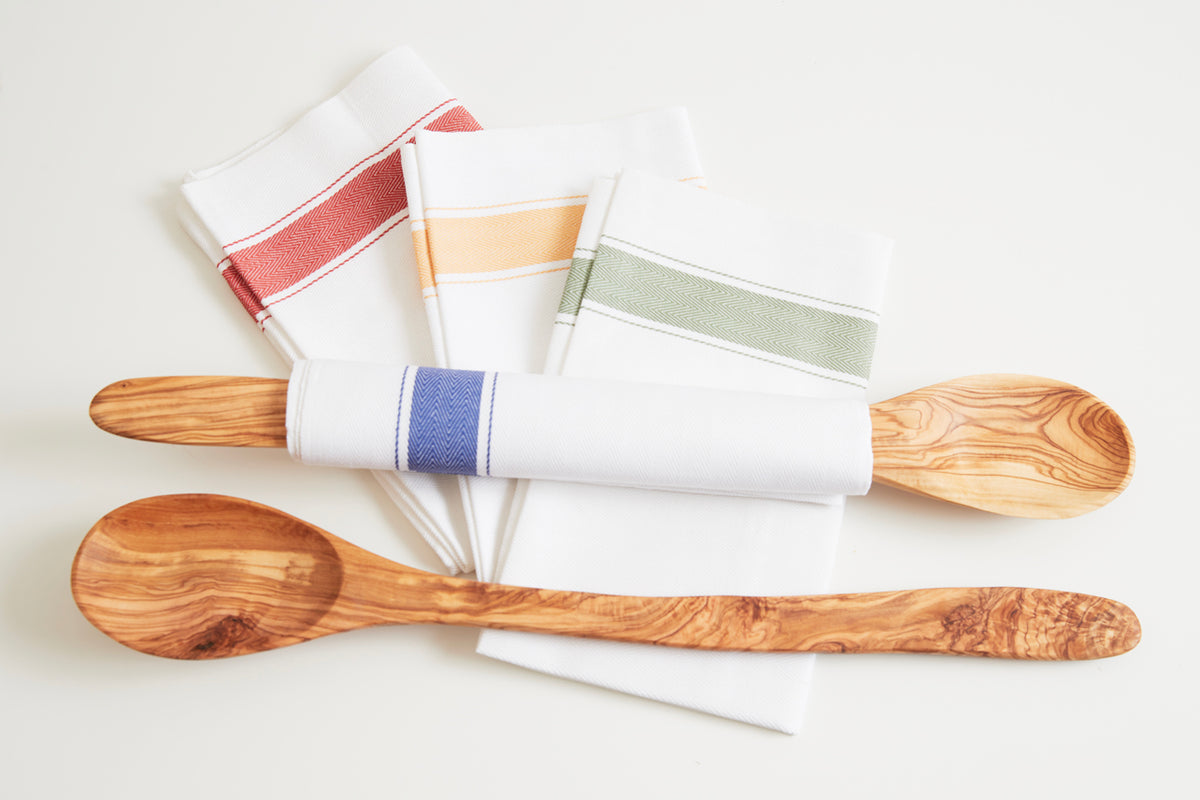 Three wooden spoons with olive grain pattern and white cloth napkins with colored stripes.