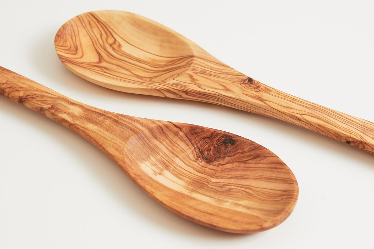 Two wooden spoons with natural grain patterns and rounded bowls, crafted from light to medium brown olivewood.
