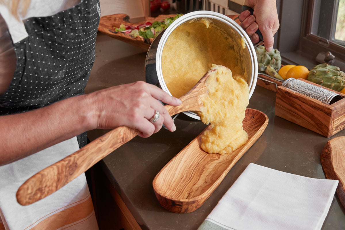 Wooden spoon with wide, flat blade spreading polenta from pot onto wooden board.