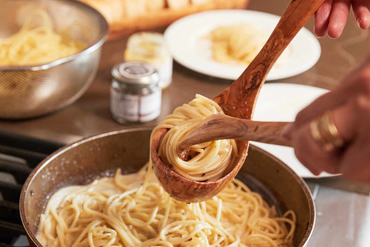 Brown wooden ladle lifting cooked spaghetti from a pot during pasta preparation.