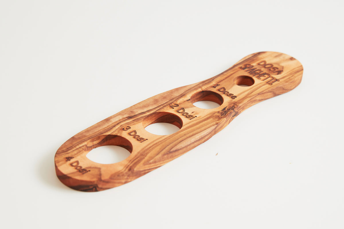 Wooden spaghetti measurer with four circular cutouts of varying sizes and engraved portion markings on handle.