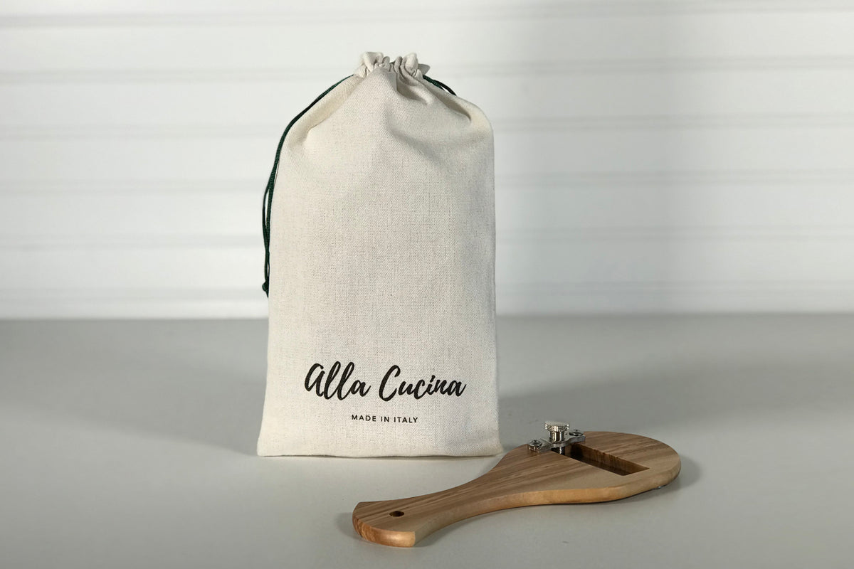 Wooden truffle slicer with metal blade and cream cotton storage pouch labeled "Alla Cucina."