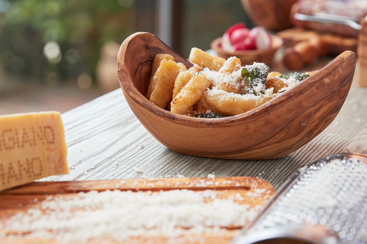 Wooden oval bowl with natural grain holding fried pastries dusted with powdered sugar and herbs.
