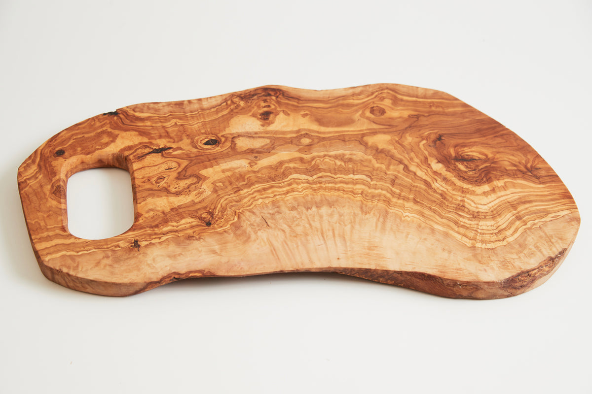 Large olive wood cutting board with organic shape, handle cutout, and natural grain patterns visible throughout.