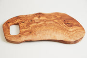 Large olive wood cutting board with organic shape, handle cutout, and natural grain patterns visible throughout.