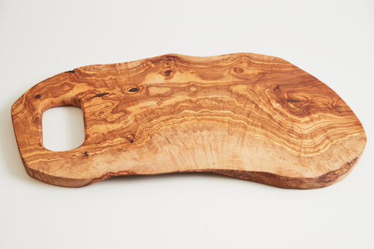 Large olive wood cutting board with organic shape, handle cutout, and natural grain patterns visible throughout.