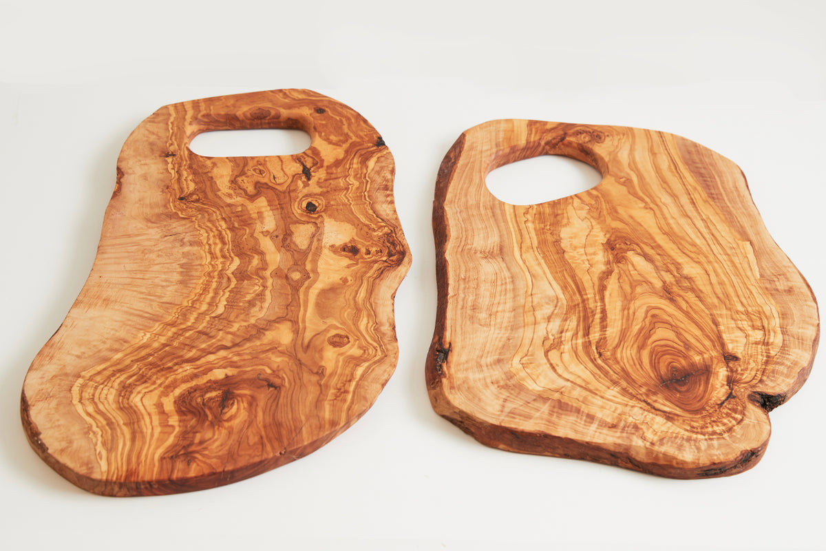Two large olivewood cutting boards with irregular edges, natural grain patterns, and handle cutouts.