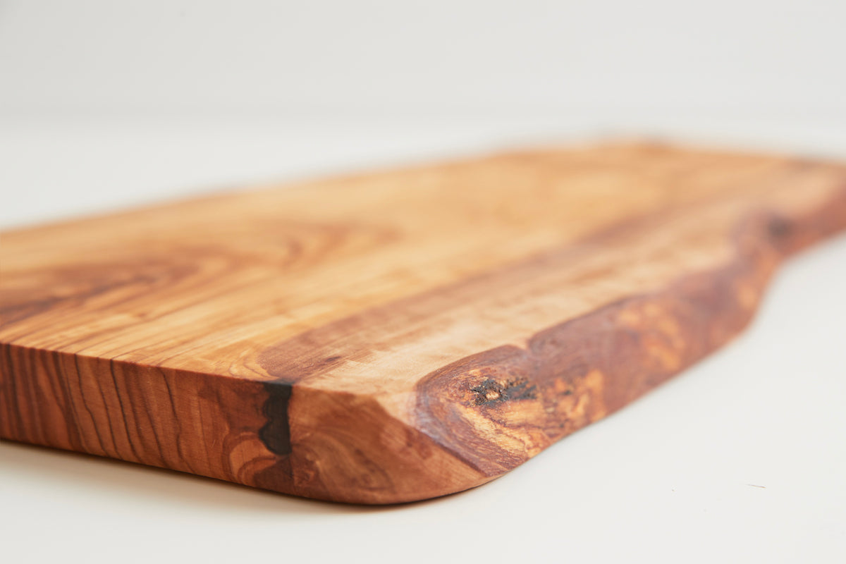 Oval olive wood cutting board with rounded edges and a circular hole for hanging, displaying natural wood grain and color var