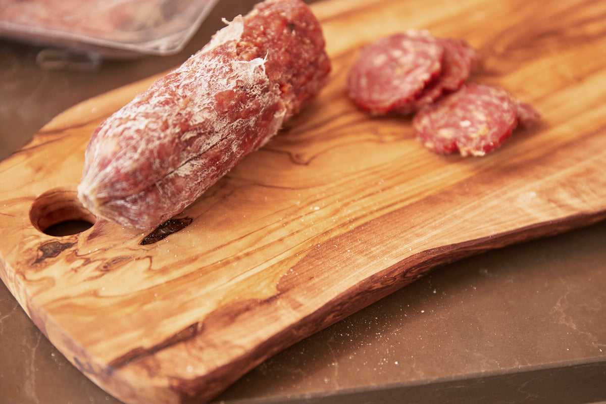 Olivewood charcuterie board with hole, displaying sliced salami and cured meats.