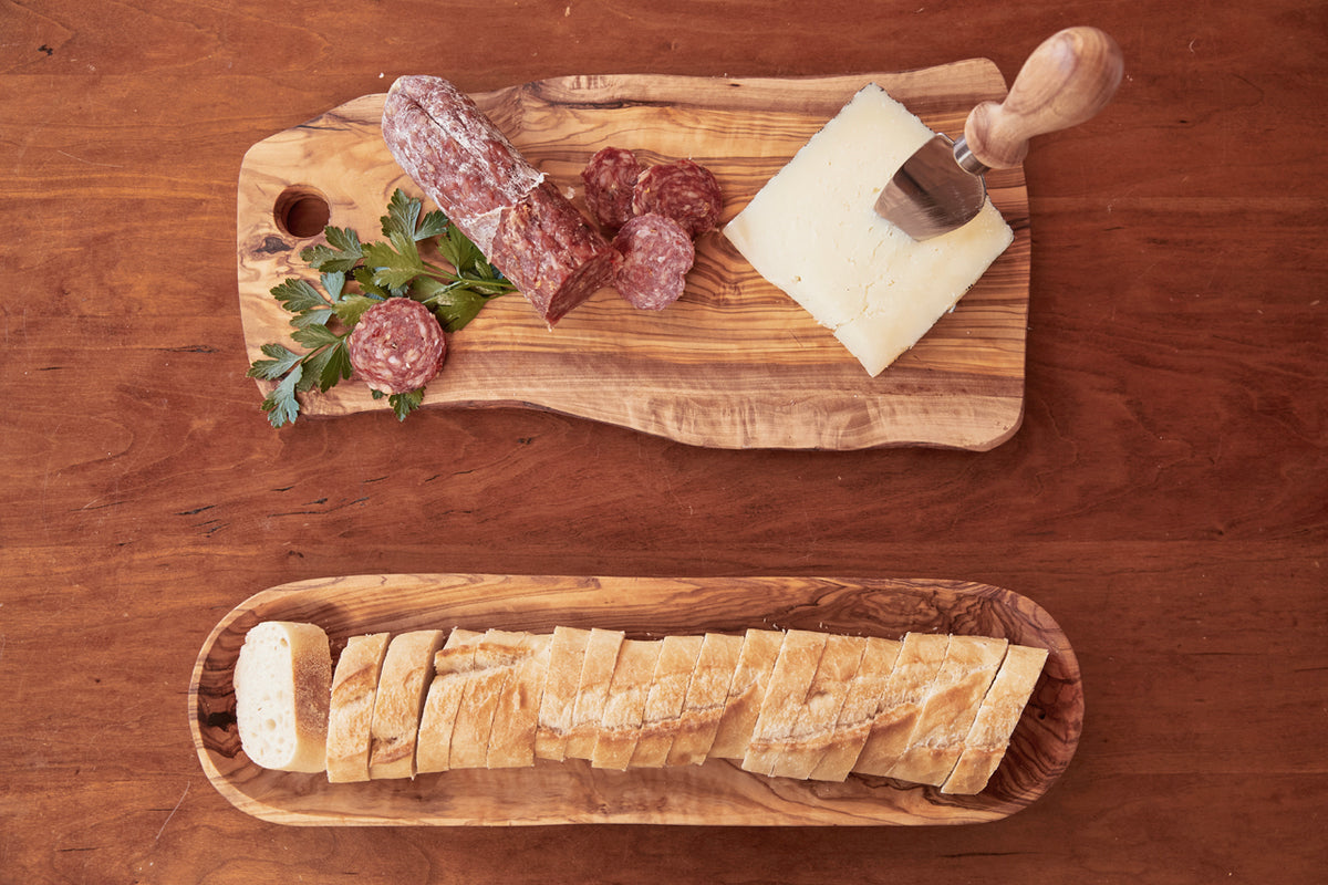 Olive wood charcuterie boards with salami, cheese, bread, and parsley arranged on wooden surface.