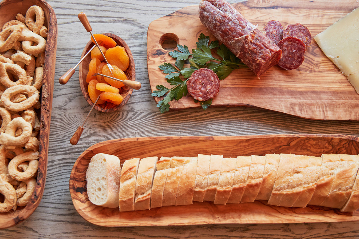Light wood charcuterie board with circular hole, displaying cured meats, cheese, bread, pretzels, and dried apricots.