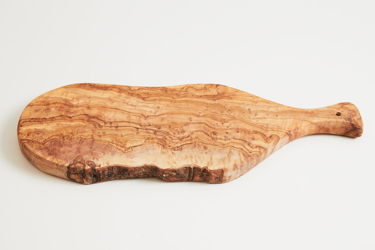 Oval olive wood charcuterie board with paddle handle and natural grain patterns on white background.