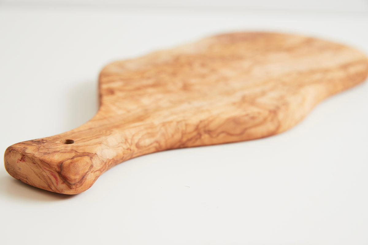 Oval olivewood board with paddle-shaped handle and natural wood grain pattern.