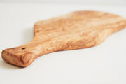 Oval olivewood board with paddle-shaped handle and natural wood grain pattern.
