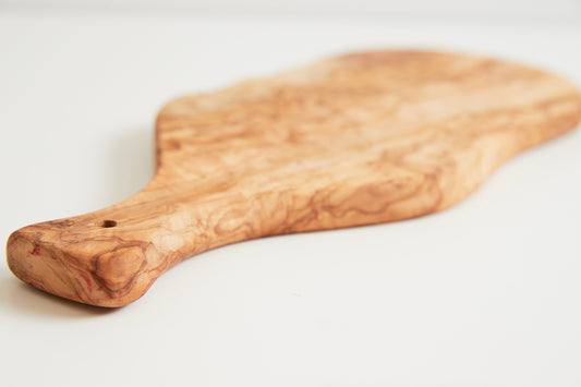 Oval olivewood board with paddle-shaped handle and natural wood grain pattern.