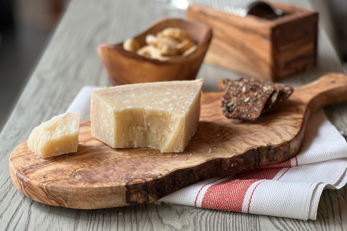 Wooden olivewood charcuterie board with paddle handle holding cheese wedges and crackers.