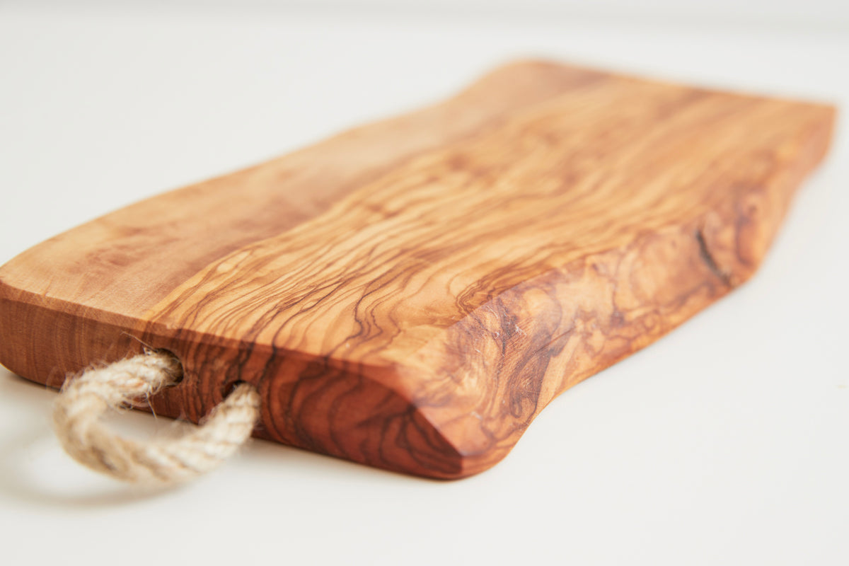 Olivewood charcuterie board with natural wood grain and attached rope handle.
