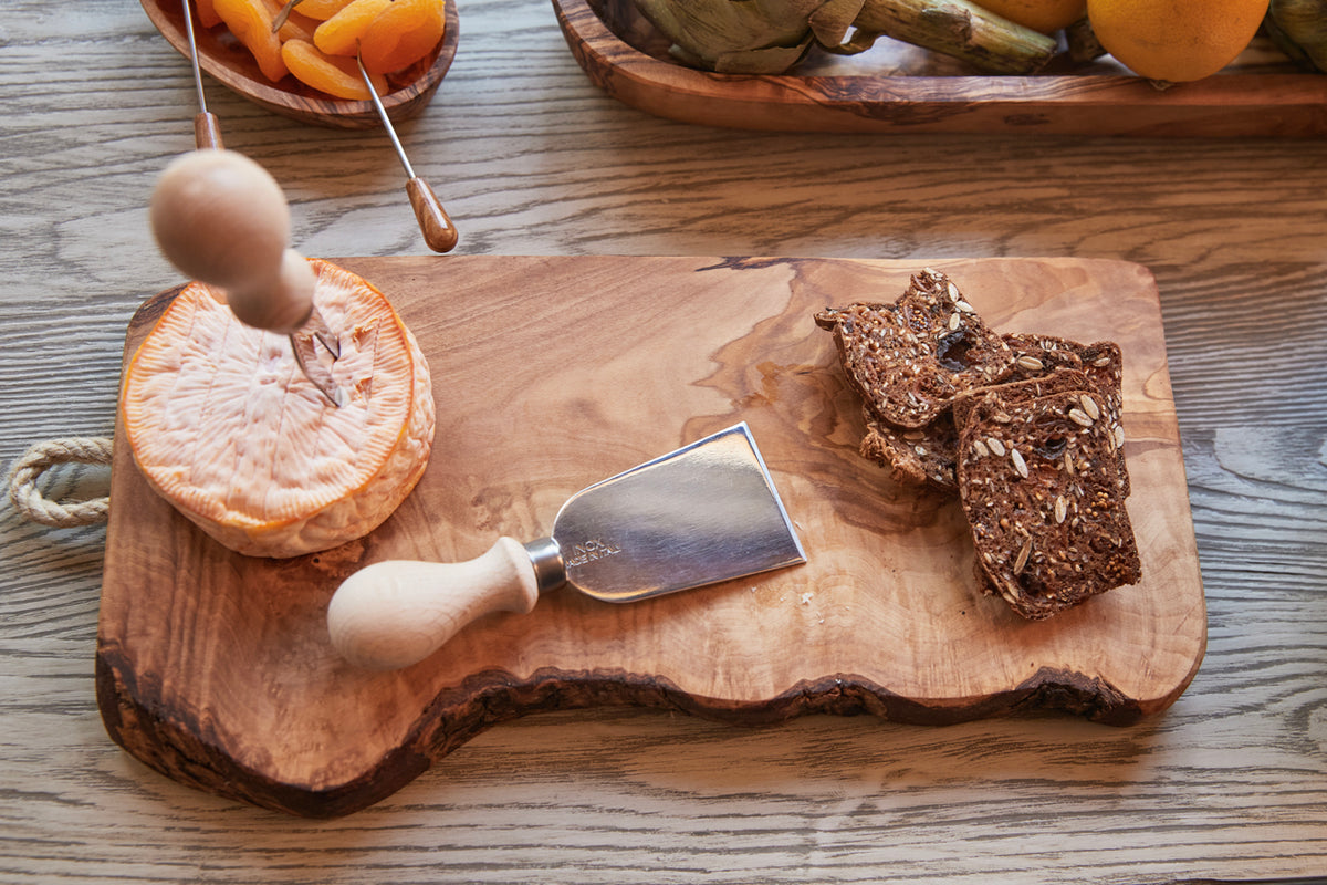 Olive wood charcuterie board with rope handle, cheese knife, and citrus slices displayed.