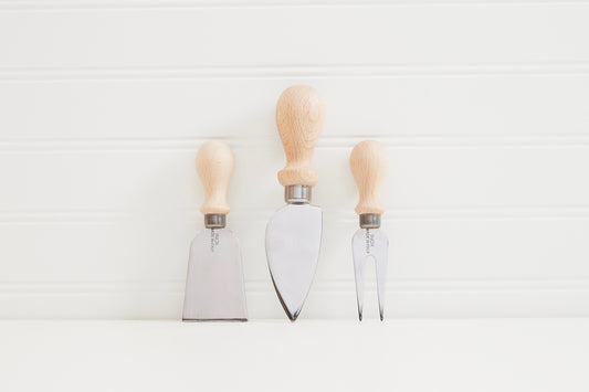 Three cheese knives with wooden handles and metal blades in different shapes: flat, pointed, and forked.