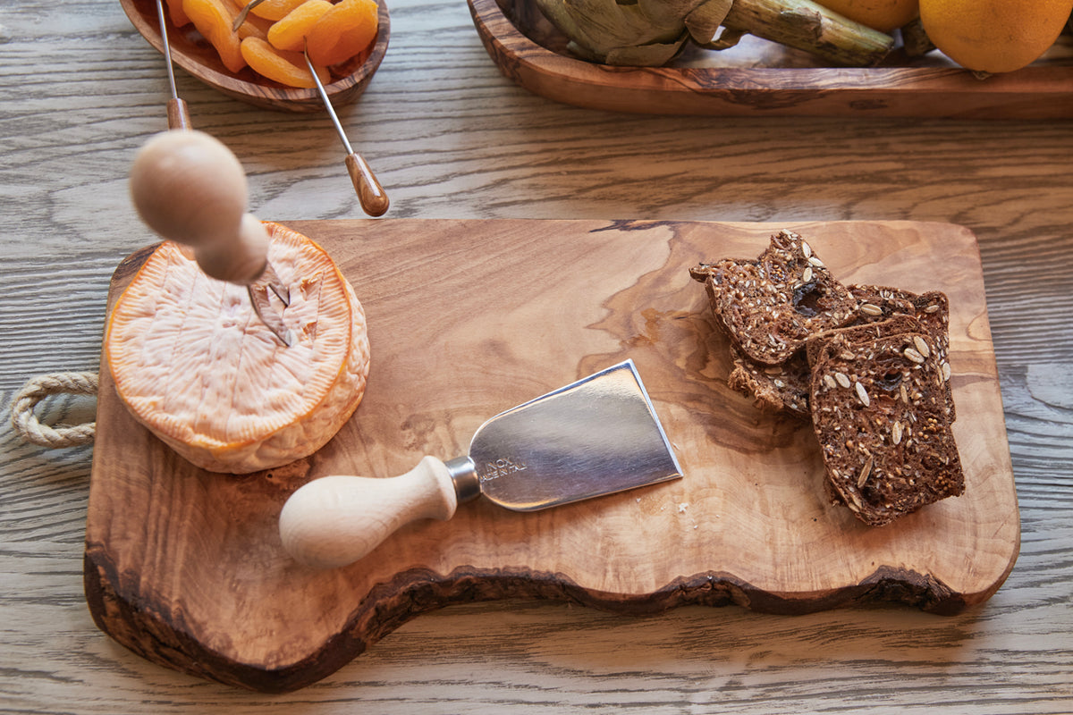 Three cheese knives with white handles displayed on a wooden board with citrus and crackers.