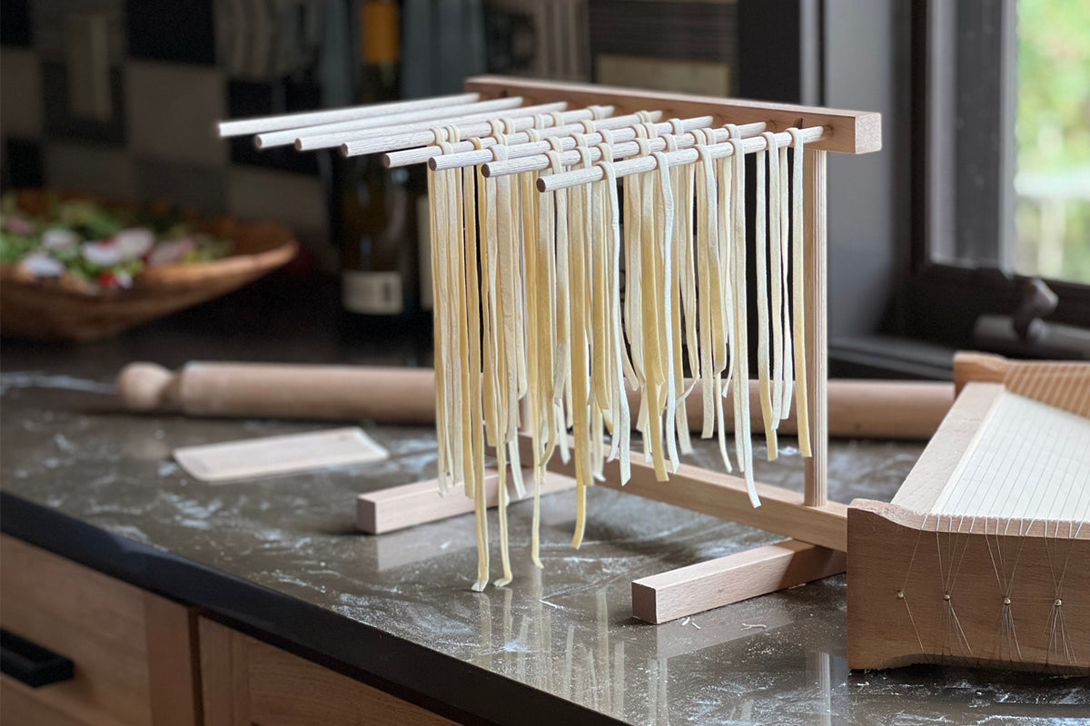 Wooden pasta drying rack with multiple horizontal rods holding strands of fresh pasta, sitting on a kitchen countertop.