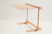 Light wood pasta drying rack with multiple horizontal rods supported by vertical frame and base stand.