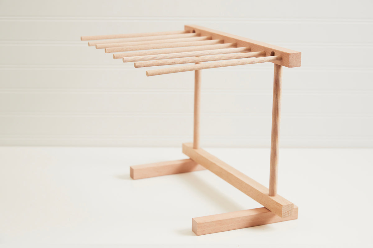 Wooden pasta drying rack with multiple horizontal dowels and rectangular base for hanging fresh pasta.