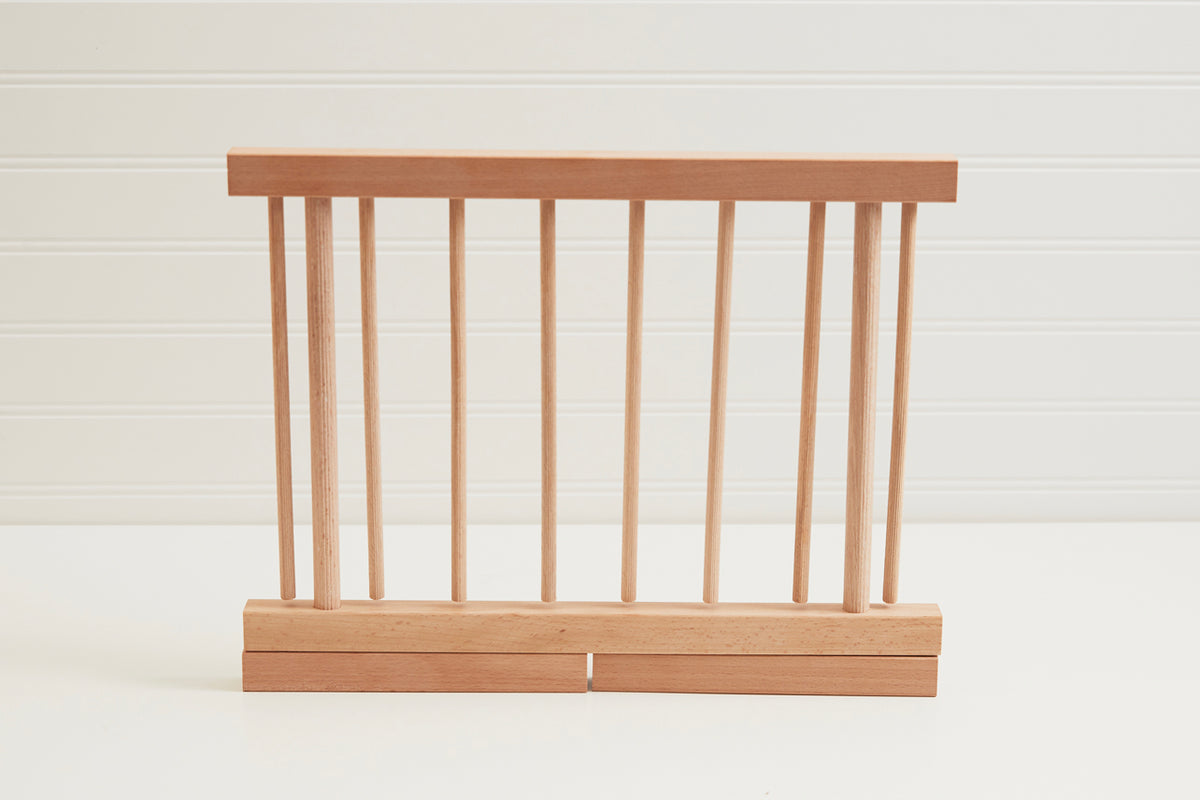 Wooden pasta drying rack with multiple vertical dowels mounted on a rectangular base with split bottom supports.