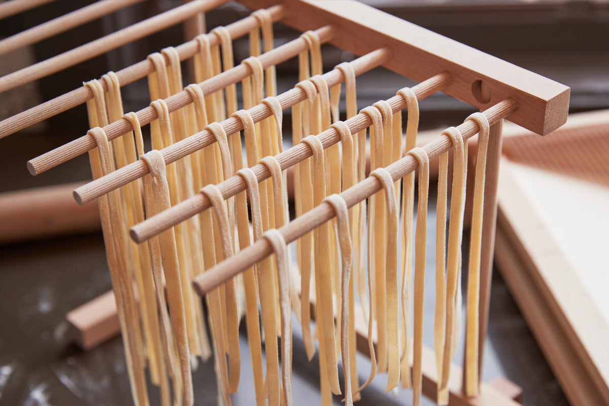 Wooden pasta drying rack with multiple horizontal rods holding fresh pasta strands draped across them.