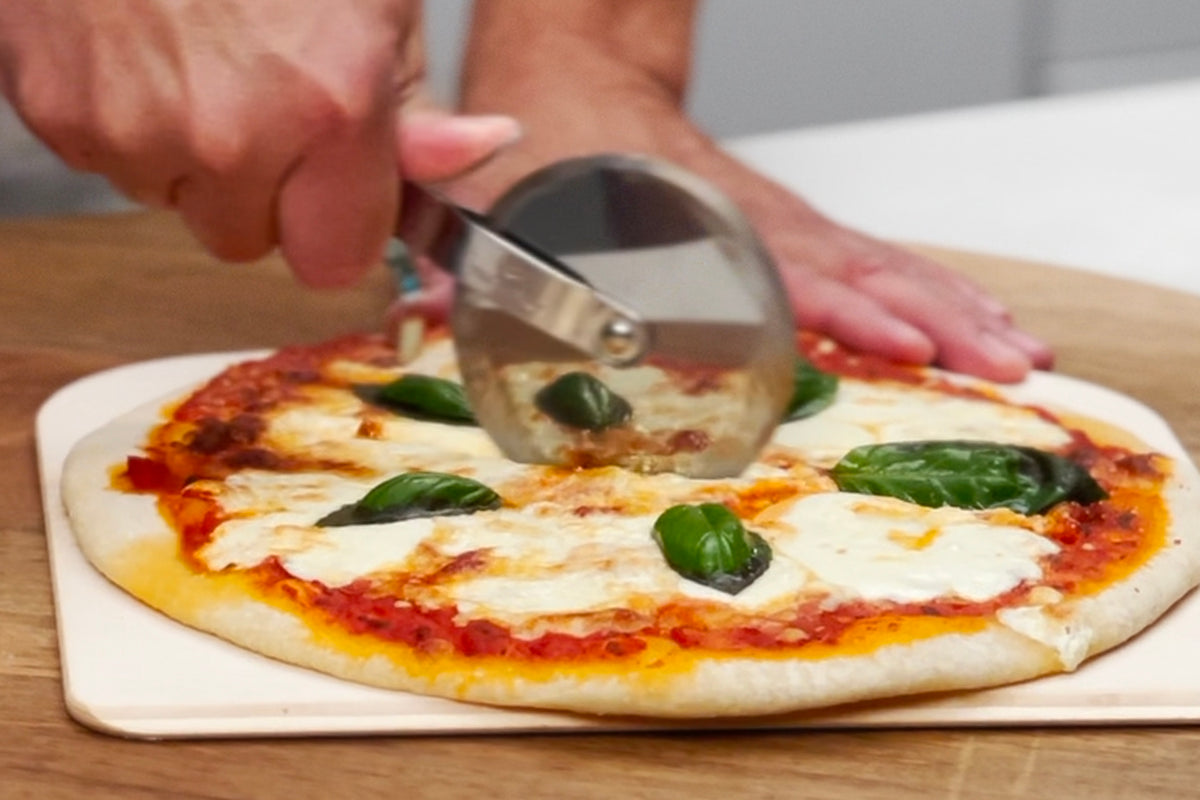Margherita pizza with red sauce, melted cheese, and basil leaves on white plate being sliced.