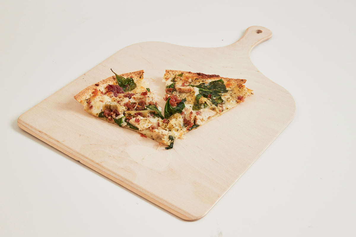 Two slices of pizza with cheese, bacon, and basil leaves on a wooden serving board.