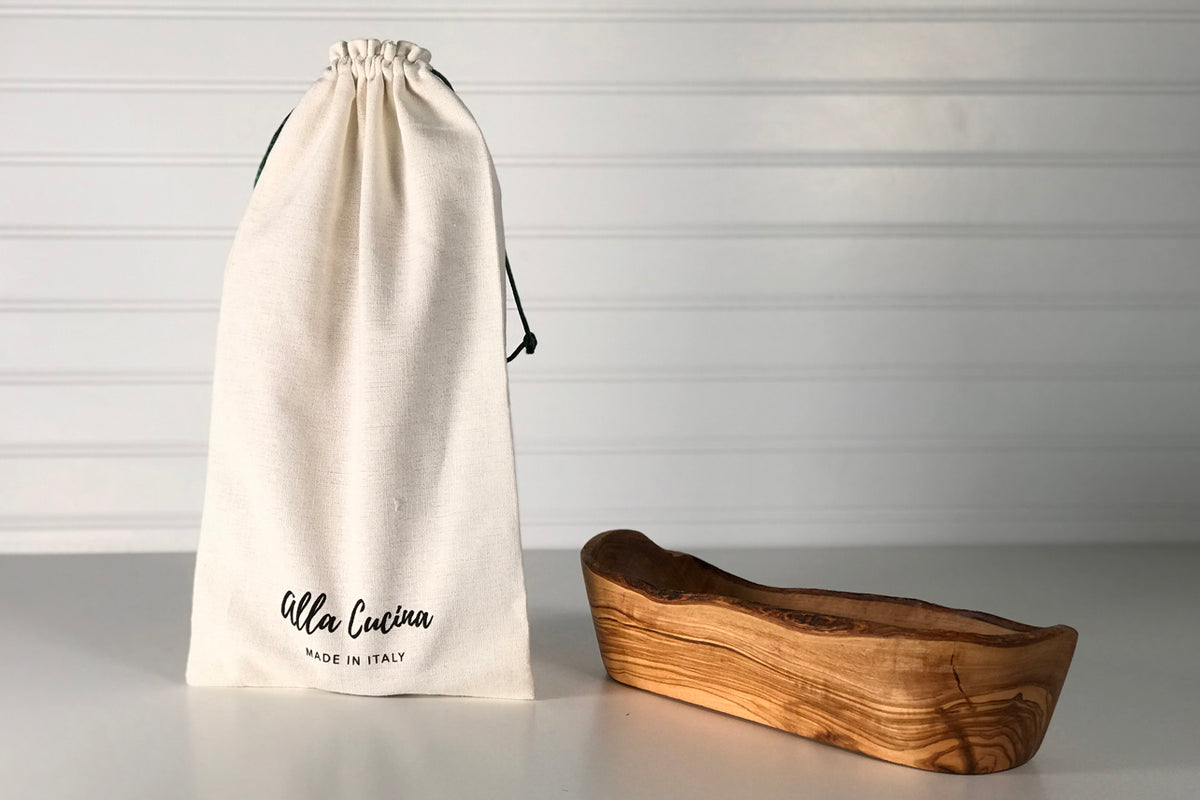 Wooden boat-shaped bowl with natural live edge in warm brown tones, displayed next to cream drawstring storage pouch.