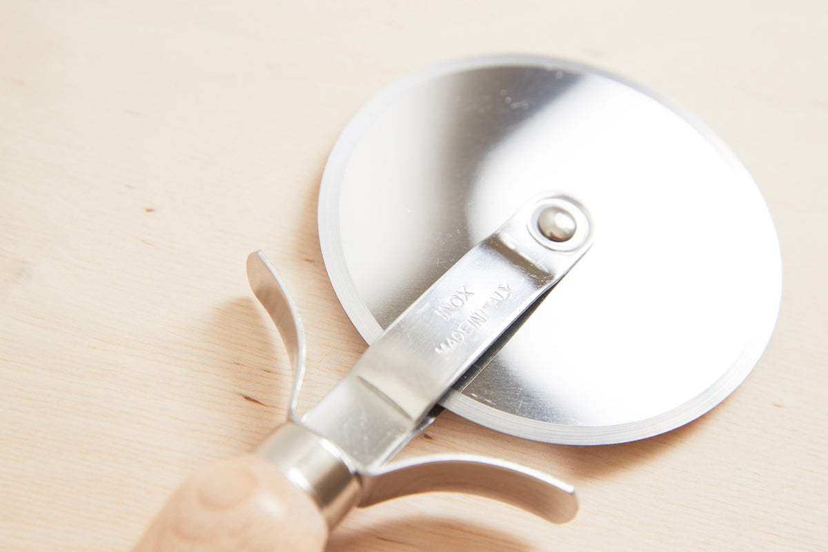 Pizza slicer with stainless steel cutting wheel and beechwood handle on light wood surface.